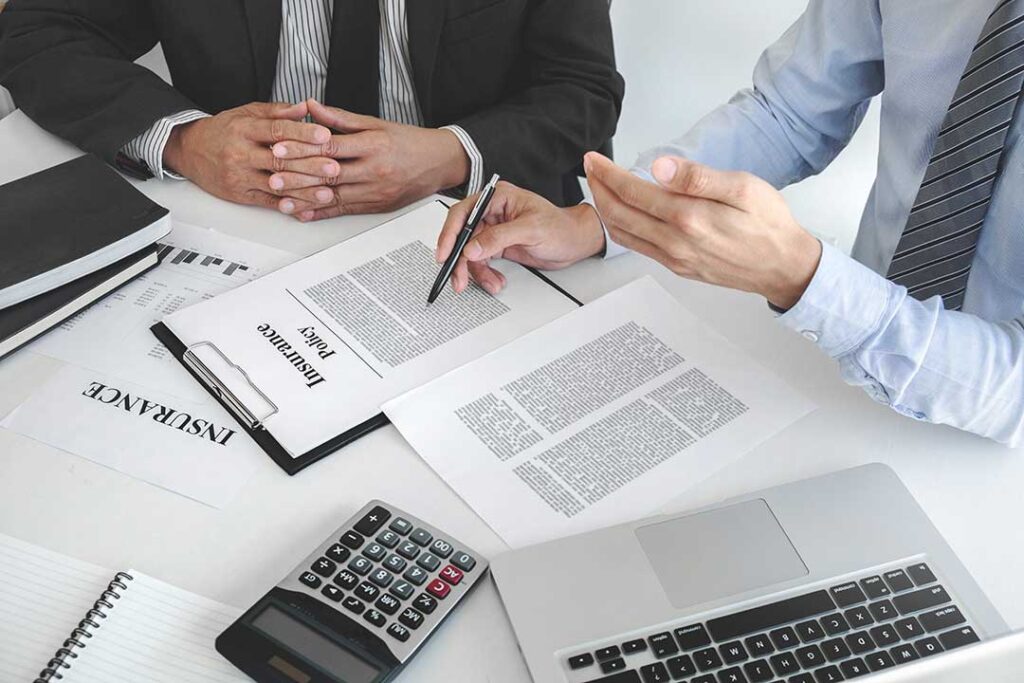 Homeowners review an insurance policy beside a calculator and emergency savings budget at a kitchen table.