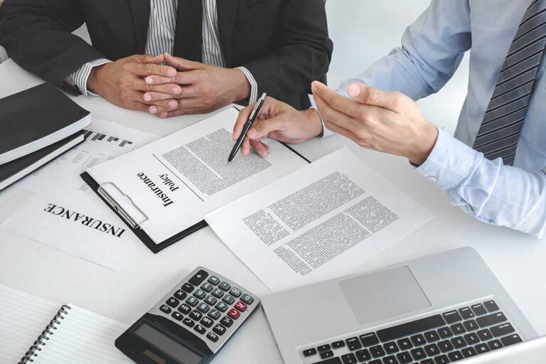 Homeowners review an insurance policy beside a calculator and emergency savings budget at a kitchen table.